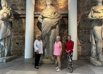 Trois femmes devant des statues allégoriques en marbre blanc.